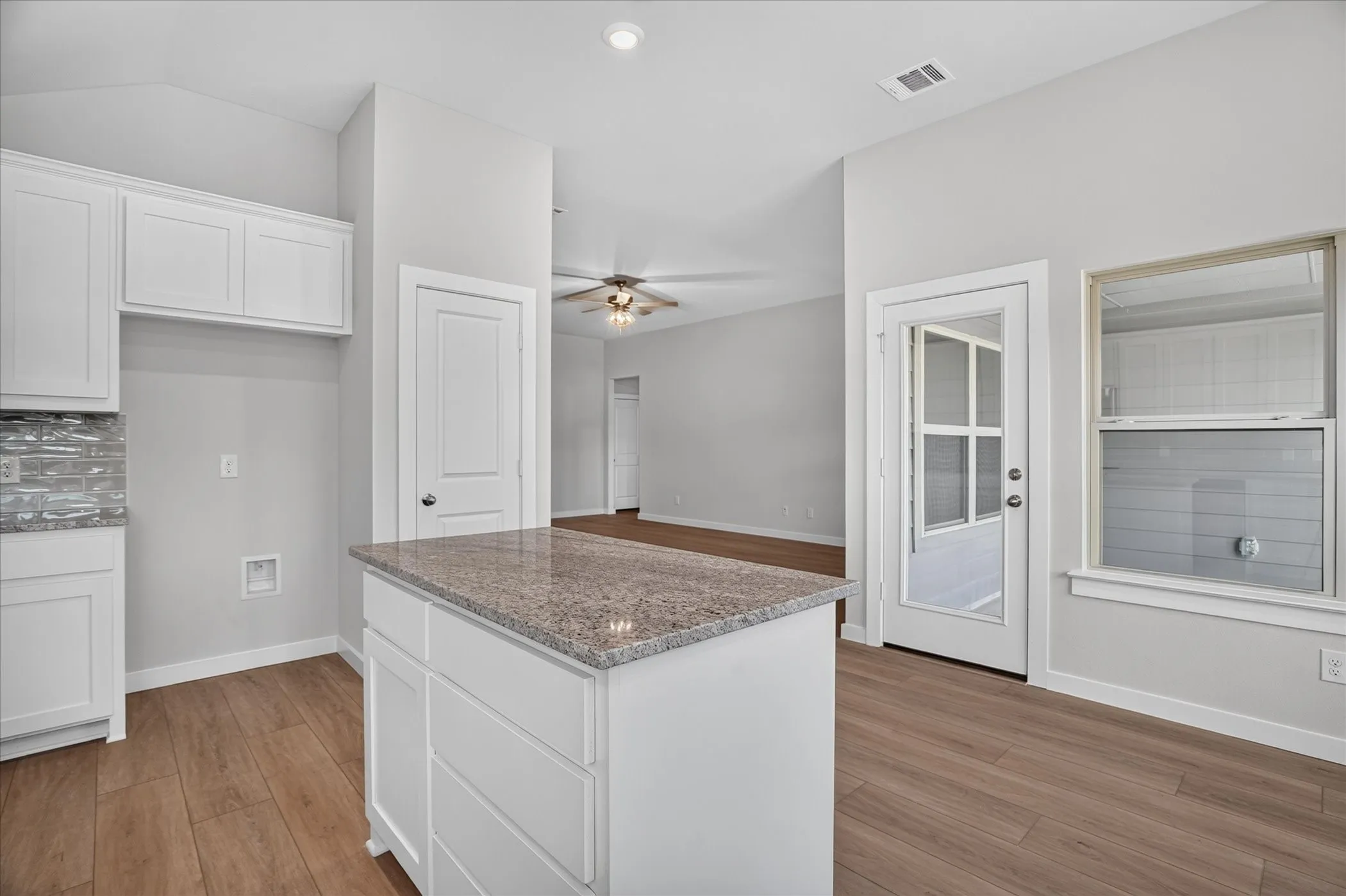 Kitchen island with a granite-style countertop, wood-finish flooring, and white cabinetry