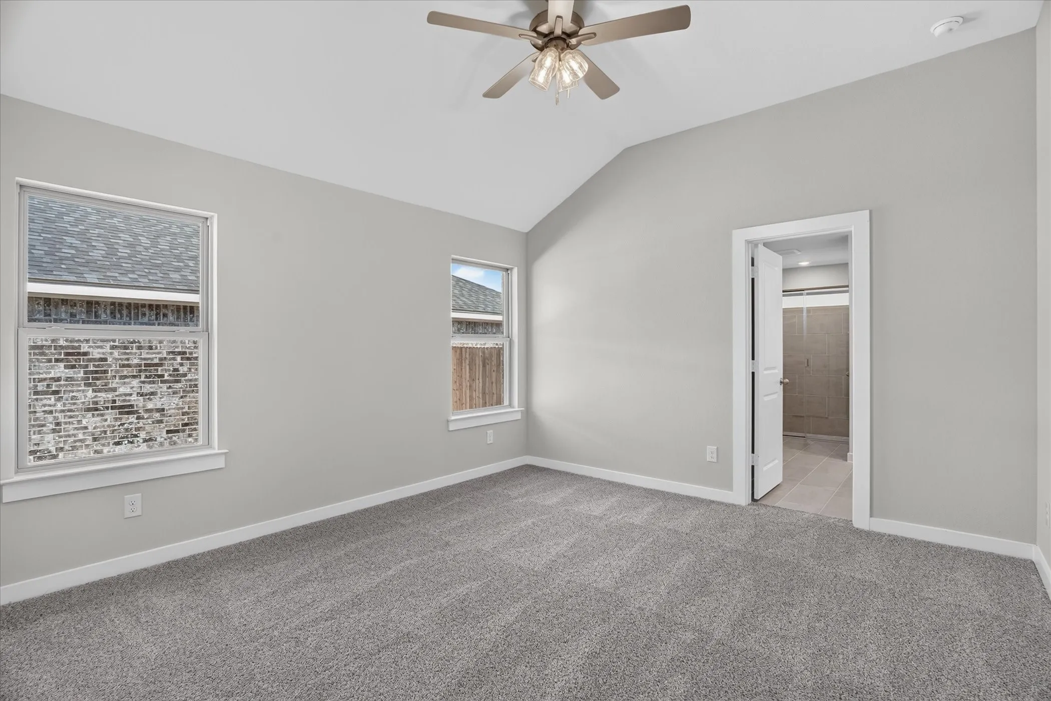 Vaulted ceiling with a ceiling fan, carpet flooring, two windows, and a doorway to an adjoining room