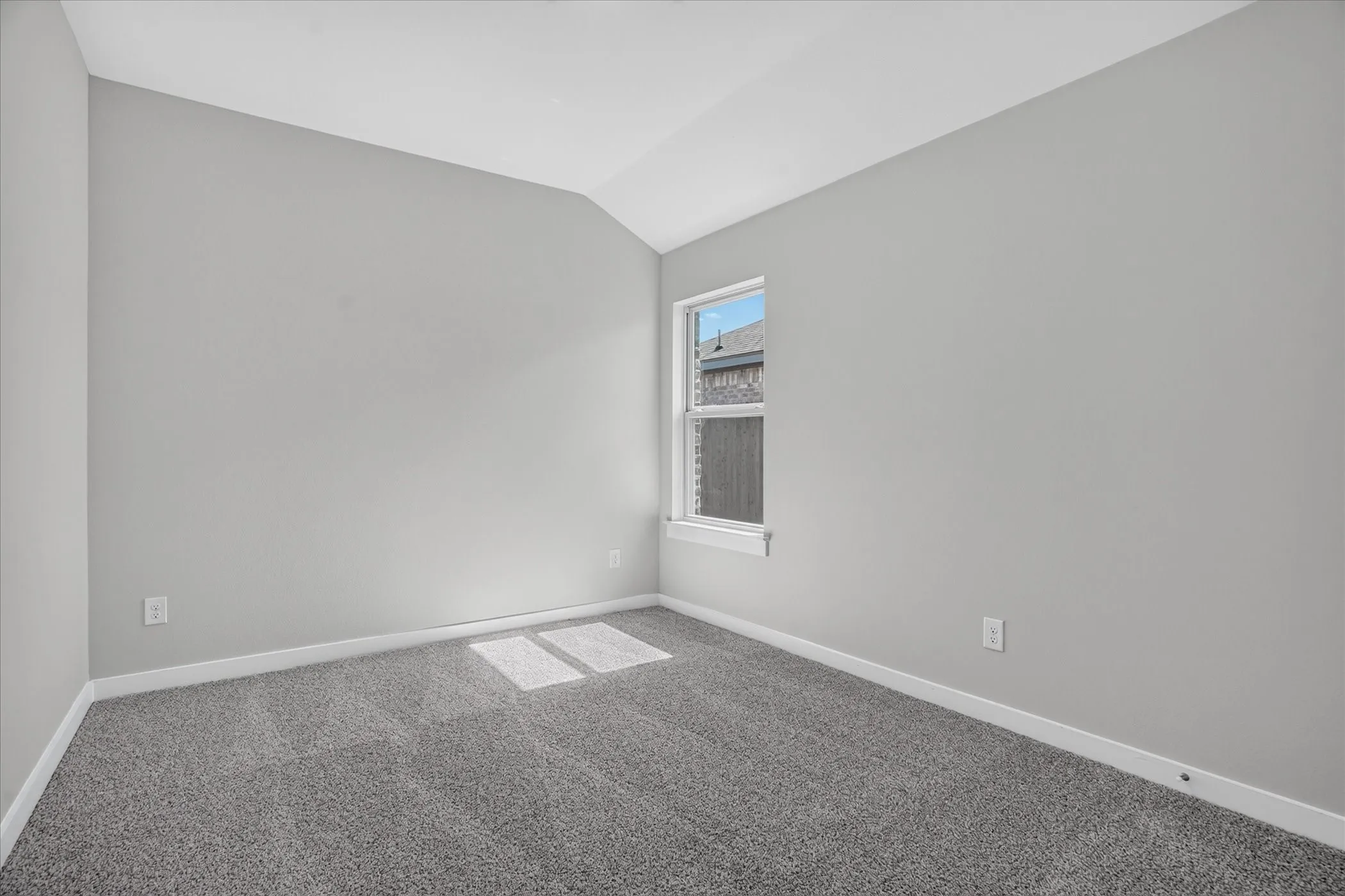 Vaulted ceiling with light gray painted walls, window with white trim, and gray carpet