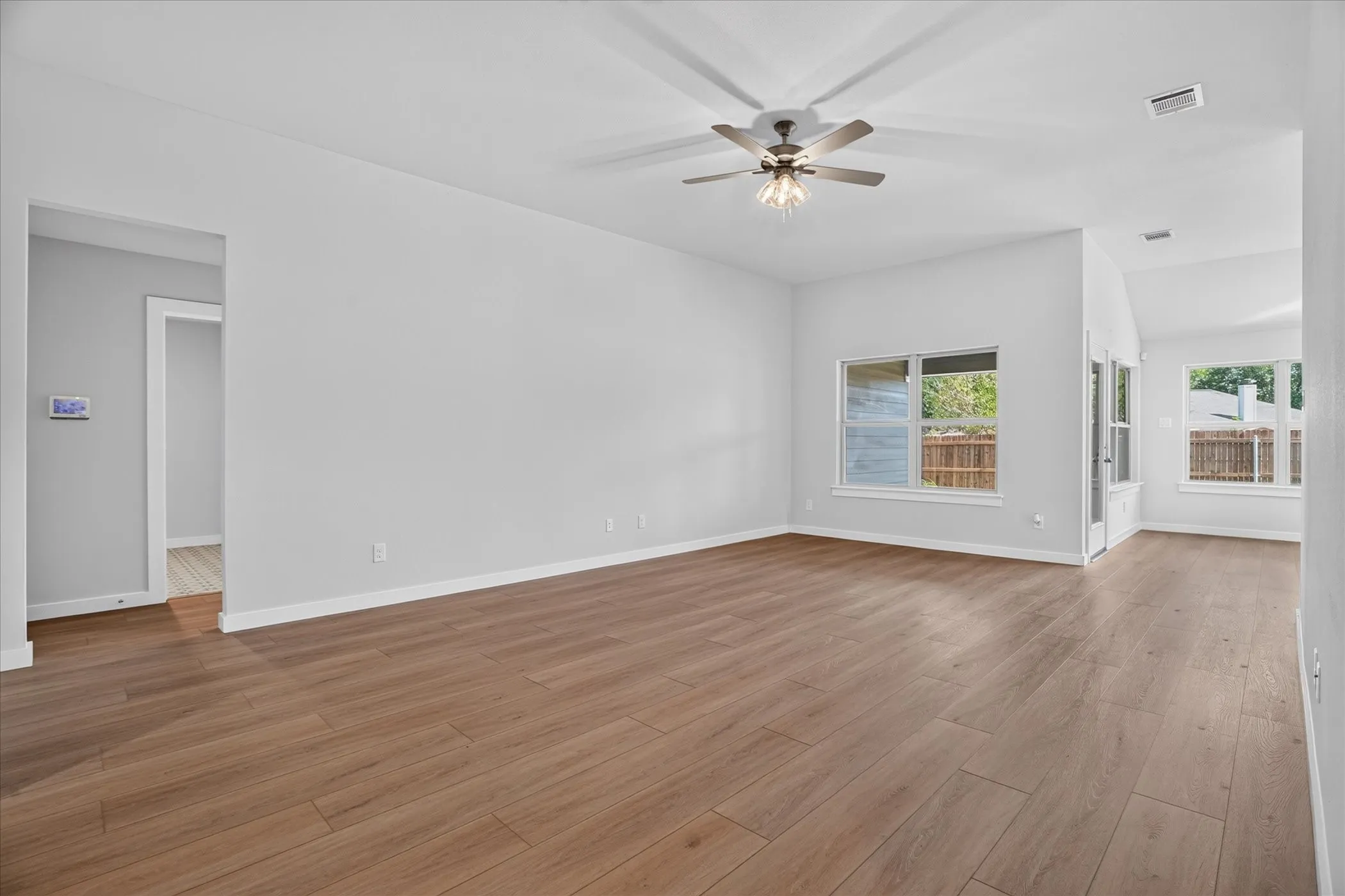 Expansive living area with wood-finish flooring, neutral wall tones, multiple windows, a ceiling fan, and recessed lighting