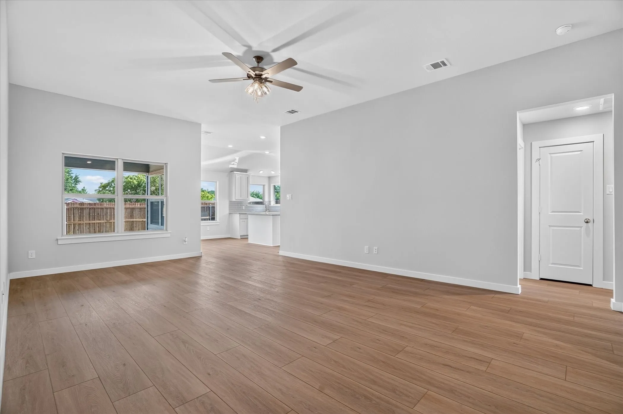 Spacious living area featuring wood-finish flooring, light gray wall tones, and a ceiling fan with integrated lighting