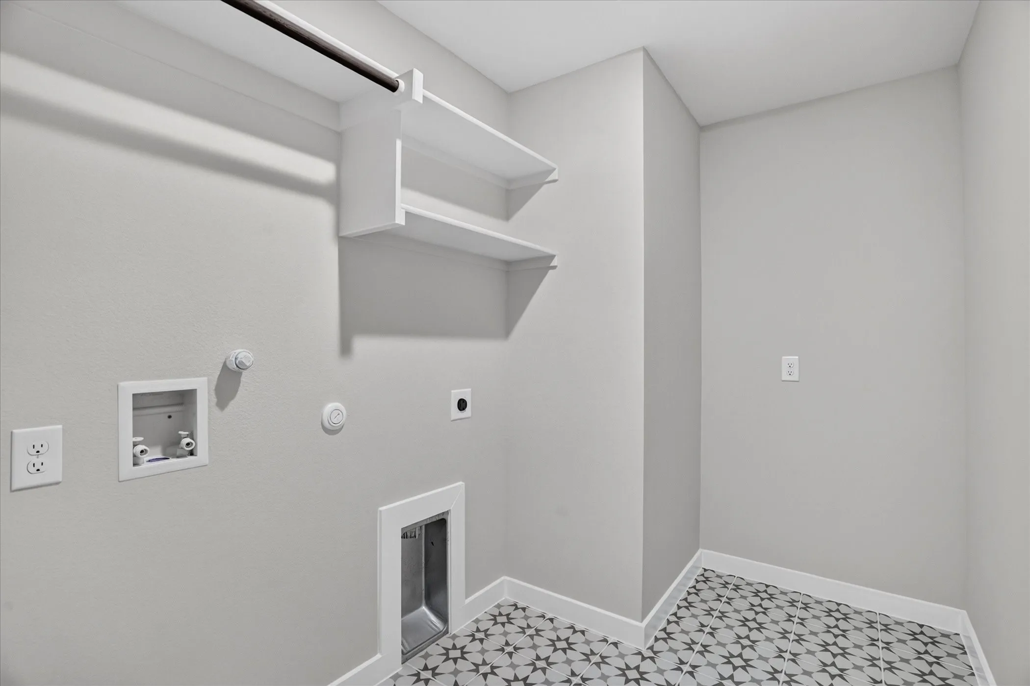 Laundry area featuring built-in shelving, a clothes hanging rod, and patterned tile flooring