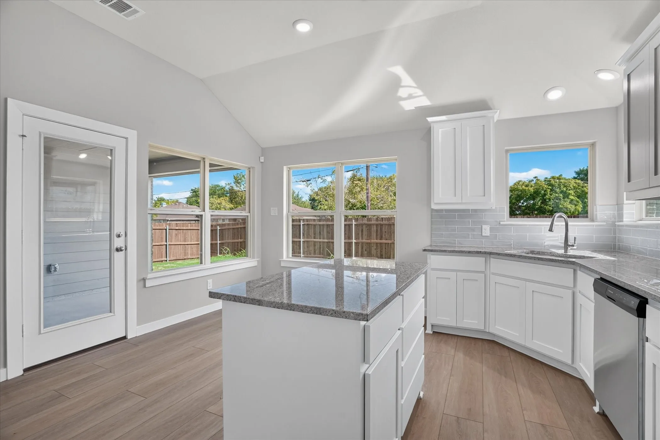 Kitchen featuring white cabinetry, gray subway tile backsplash, a center island with a granite countertop, stainless steel appliances, and wood-finish flooring