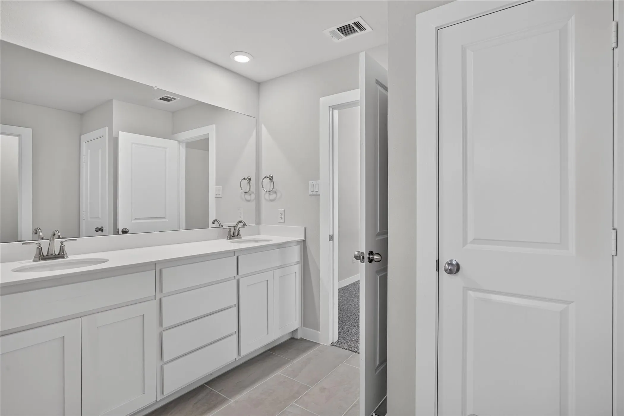 Dual vanity with integrated sinks, expansive wall-mounted mirror, recessed lighting, and tile flooring