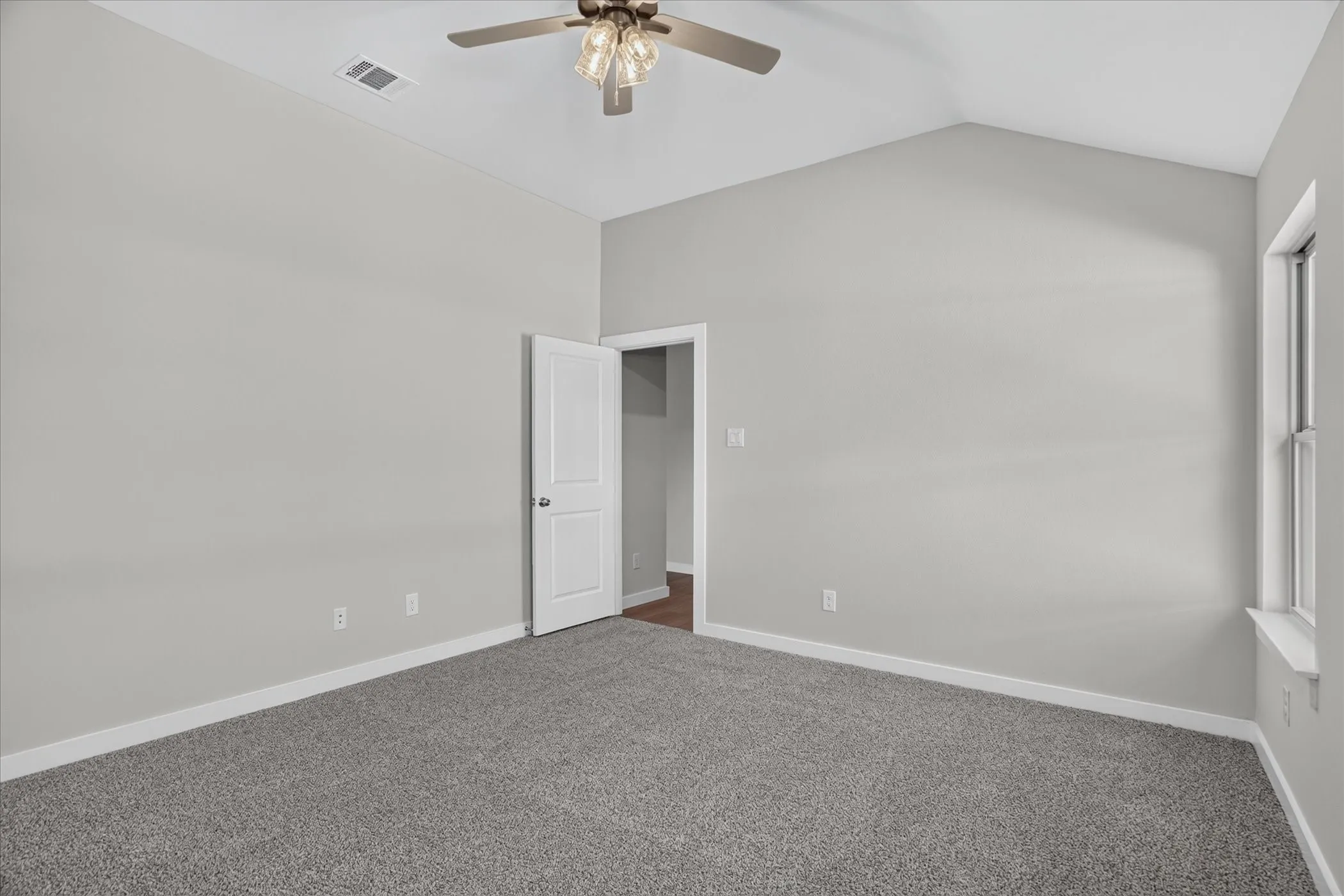 Vaulted ceiling with an attached ceiling fan, light gray wall paint, gray carpeting, and a window with white trim