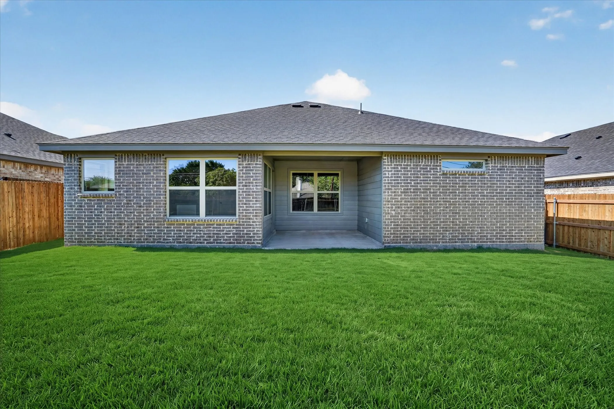 Expansive backyard with a manicured lawn, brick exterior, and covered patio