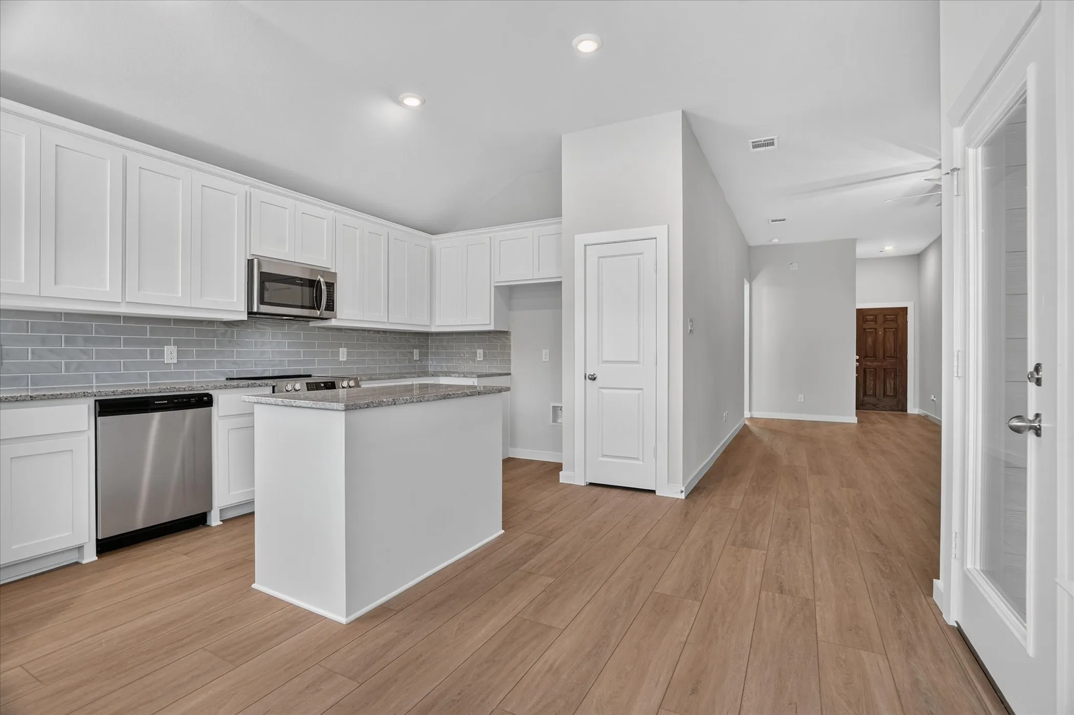 Kitchen featuring white shaker cabinetry, stainless steel appliances, a center island, gray subway tile backsplash, and wood-finish flooring