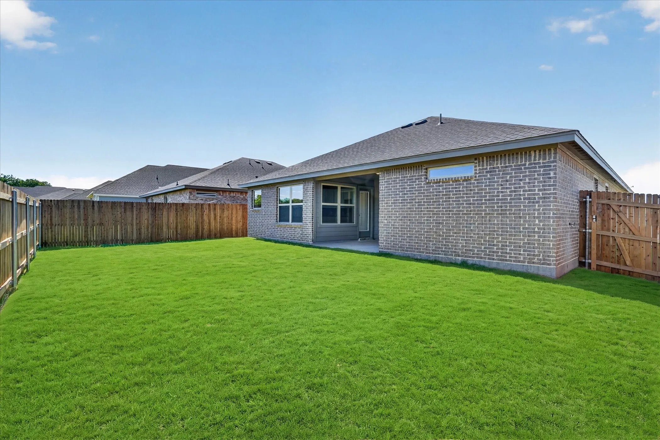 Expansive backyard featuring a manicured lawn, full perimeter wood fencing, a covered patio, and a brick exterior