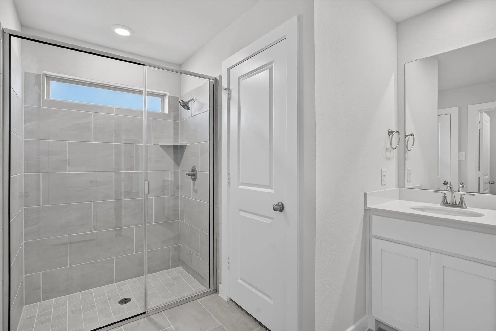 Glass-enclosed shower with a transom window and tiled walls, complemented by a single vanity with an undermount sink and chrome fixtures