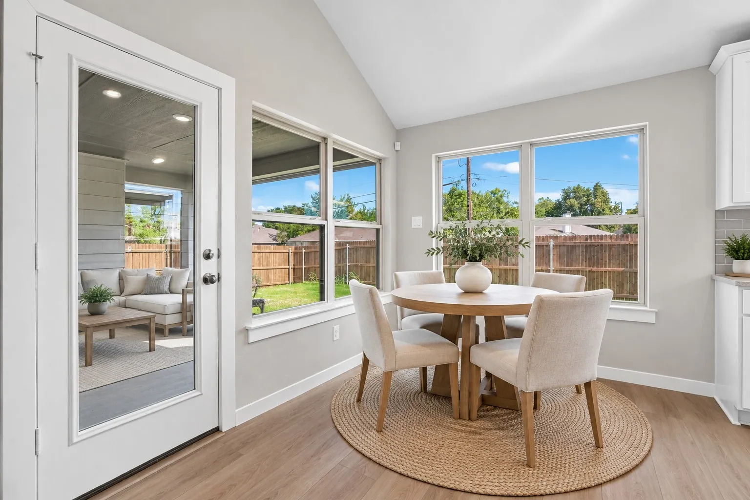 Wood-finish flooring with a full-light door, multiple large windows, and a vaulted ceiling