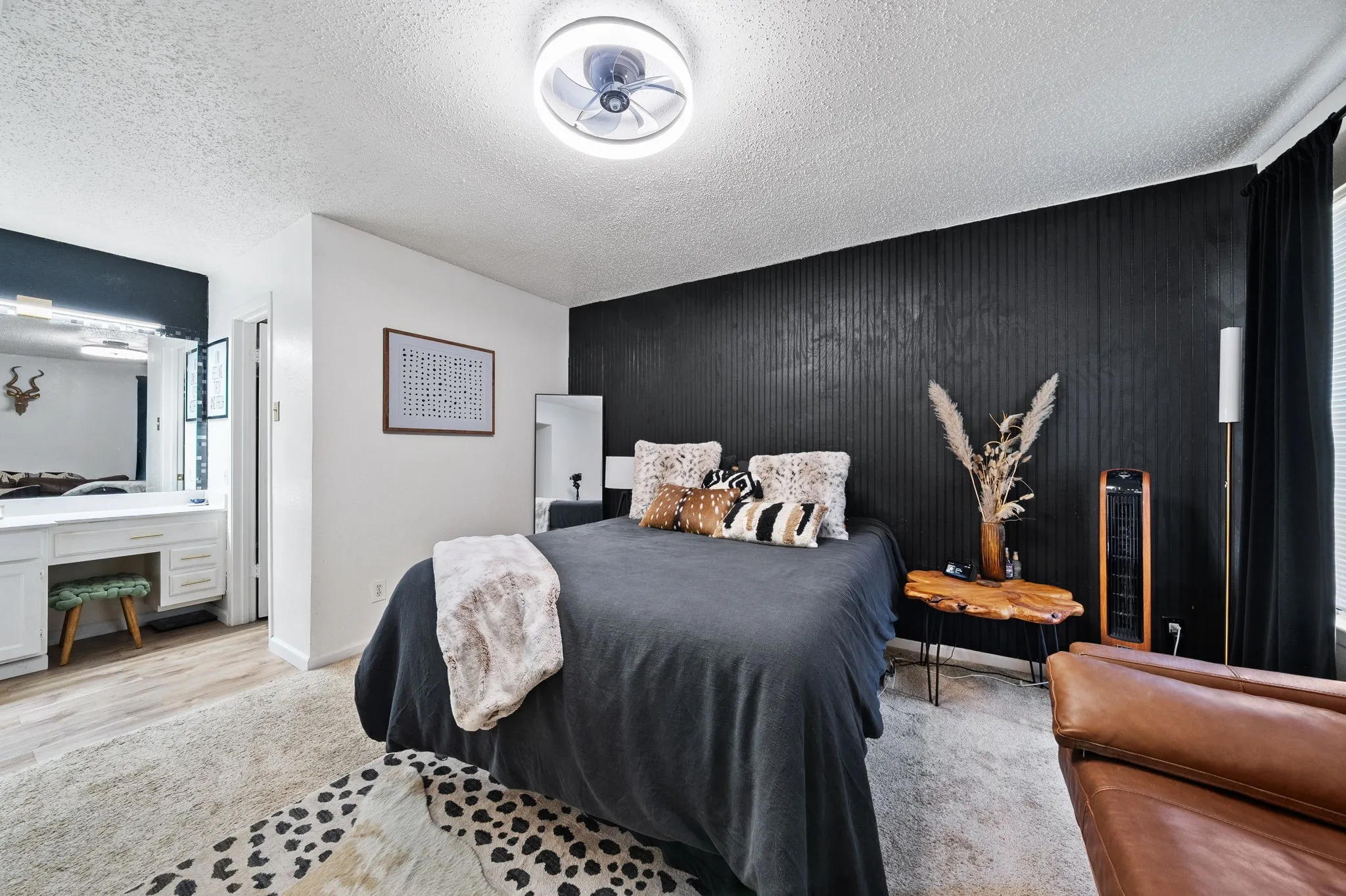 Bedroom featuring a black accent wall with vertical paneling, light-toned carpeting, and a built-in vanity with white cabinetry and a tri-fold mirror