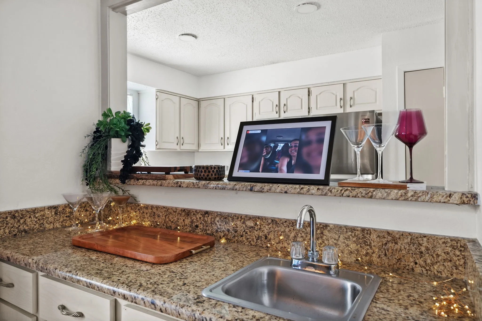 Kitchen pass-through featuring granite-style countertops, an undermount stainless steel sink with a chrome faucet, and white upper and lower cabinetry