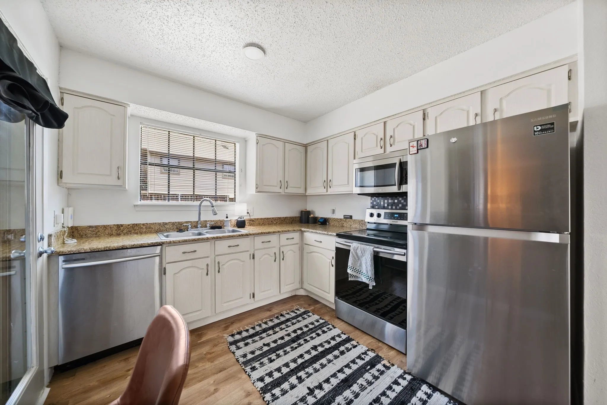 Kitchen featuring light-toned cabinetry, stainless steel appliances, granite-style countertops, and wood-finish flooring