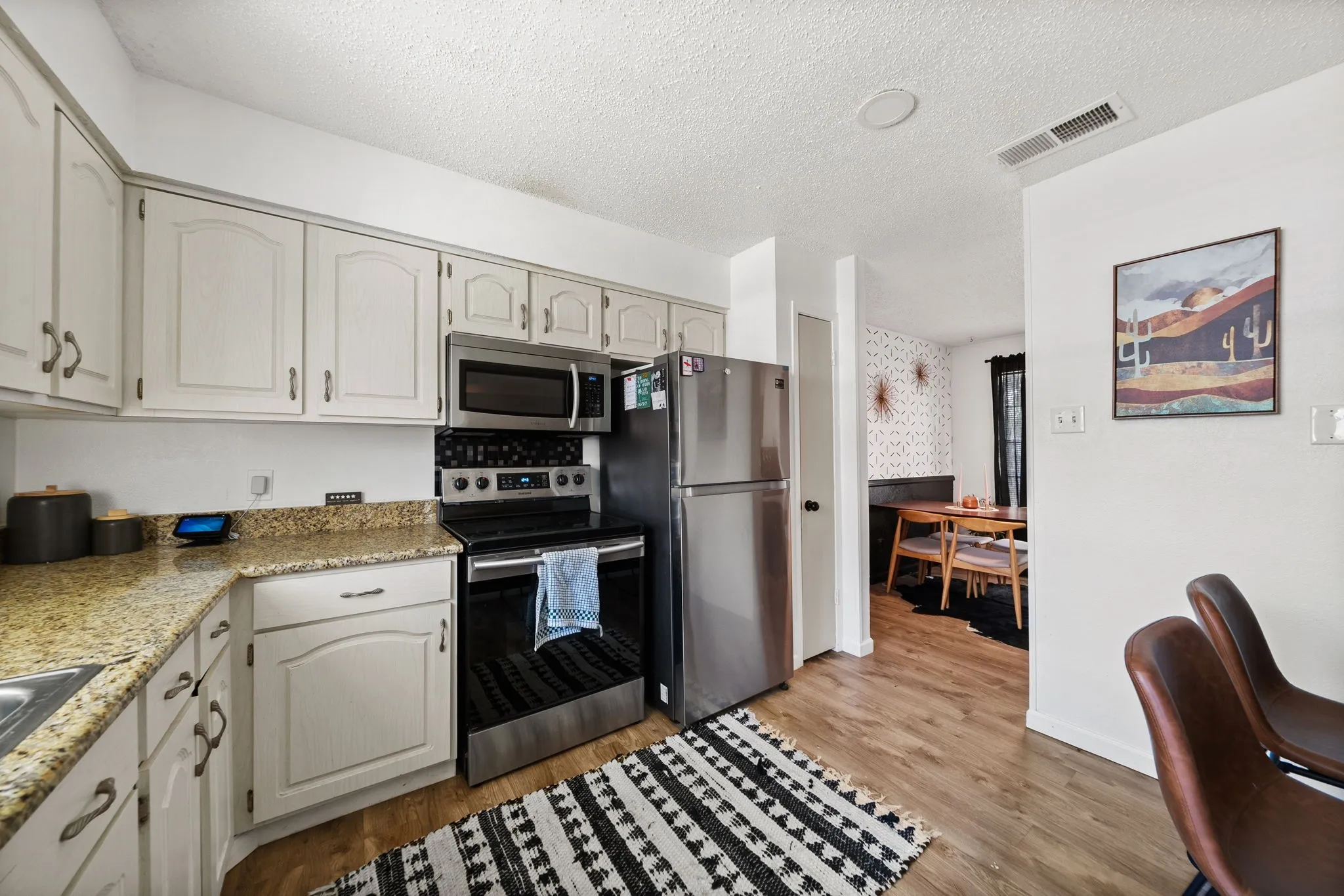 Kitchen featuring light-toned cabinetry, stainless steel appliances, granite-style countertops, and wood-finish flooring