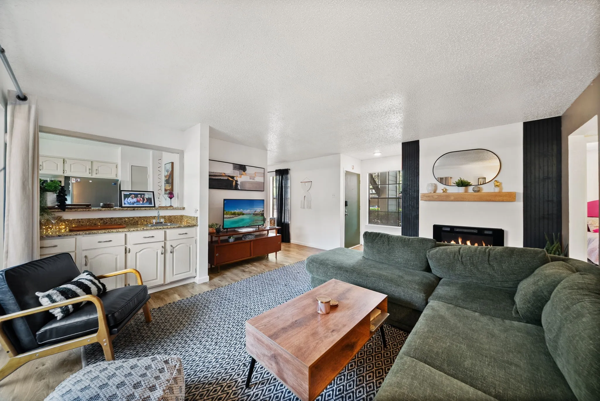 Living area featuring wood-finish flooring, a built-in wet bar with cabinetry and granite-style countertops, and a modern fireplace with a wooden mantel