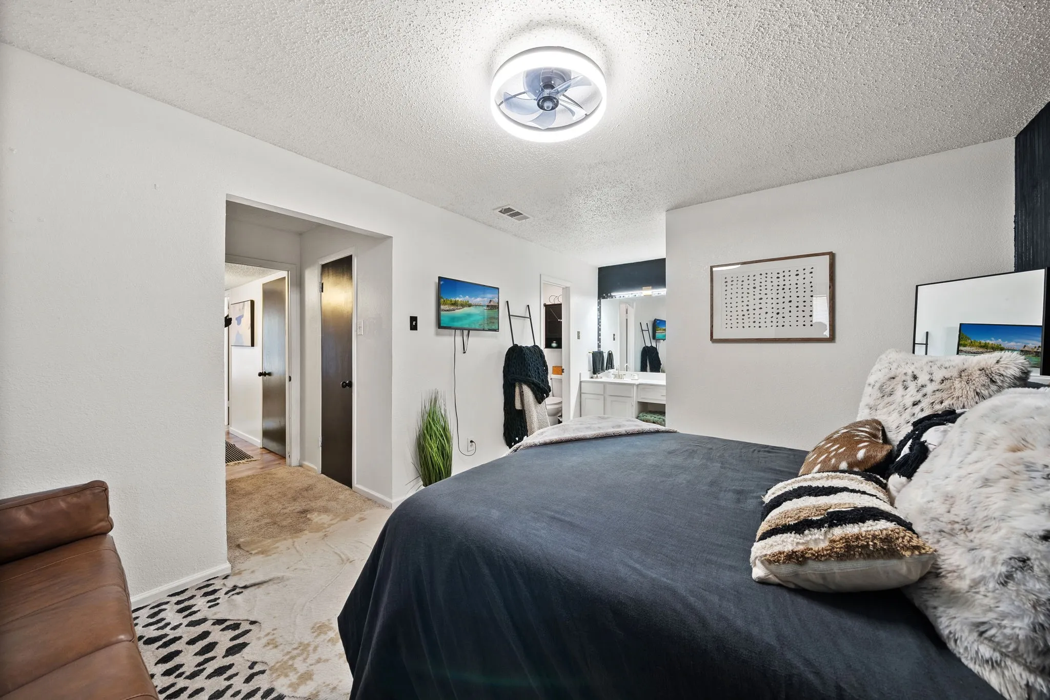 Spacious bedroom with a ceiling-mounted fan fixture, white walls, and a dedicated passage to an additional room