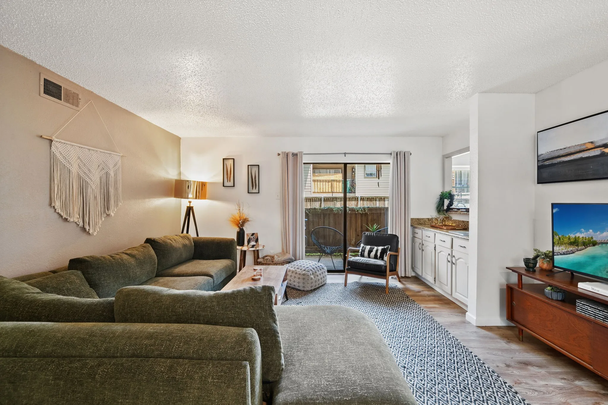 Open concept living area featuring wood-finish flooring, a glass sliding door leading to an outdoor space, and a built-in cabinetry unit with a stone-finish countertop