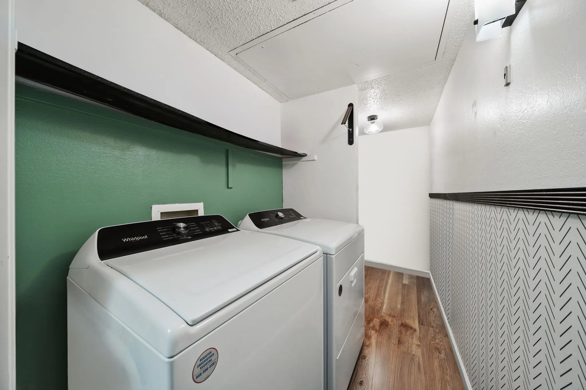 Dedicated laundry area featuring wood-finish flooring and a partial accent wall with a geometric pattern