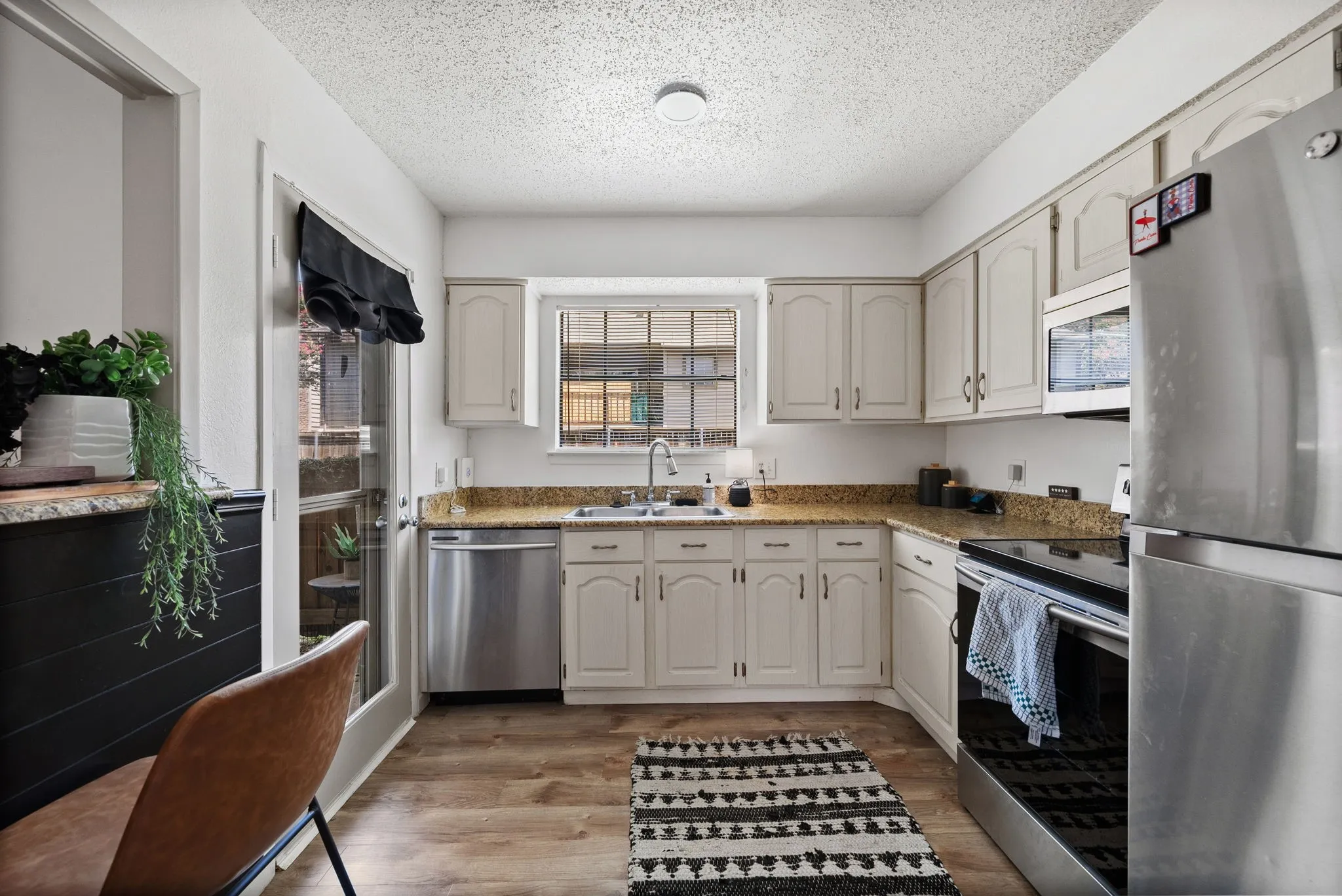 Kitchen featuring light-toned cabinetry, a stainless steel appliance suite, granite countertops, wood-finish flooring, and a glass-paneled exterior door