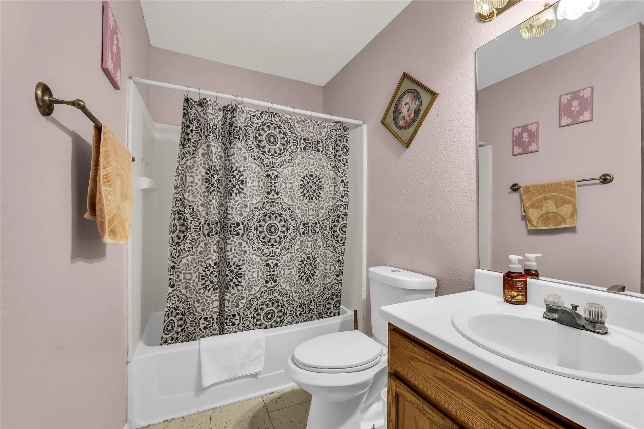 Bathroom featuring a white tub and shower combination, a white toilet, and a vanity with a wood-finish cabinet, white countertop, and integrated sink