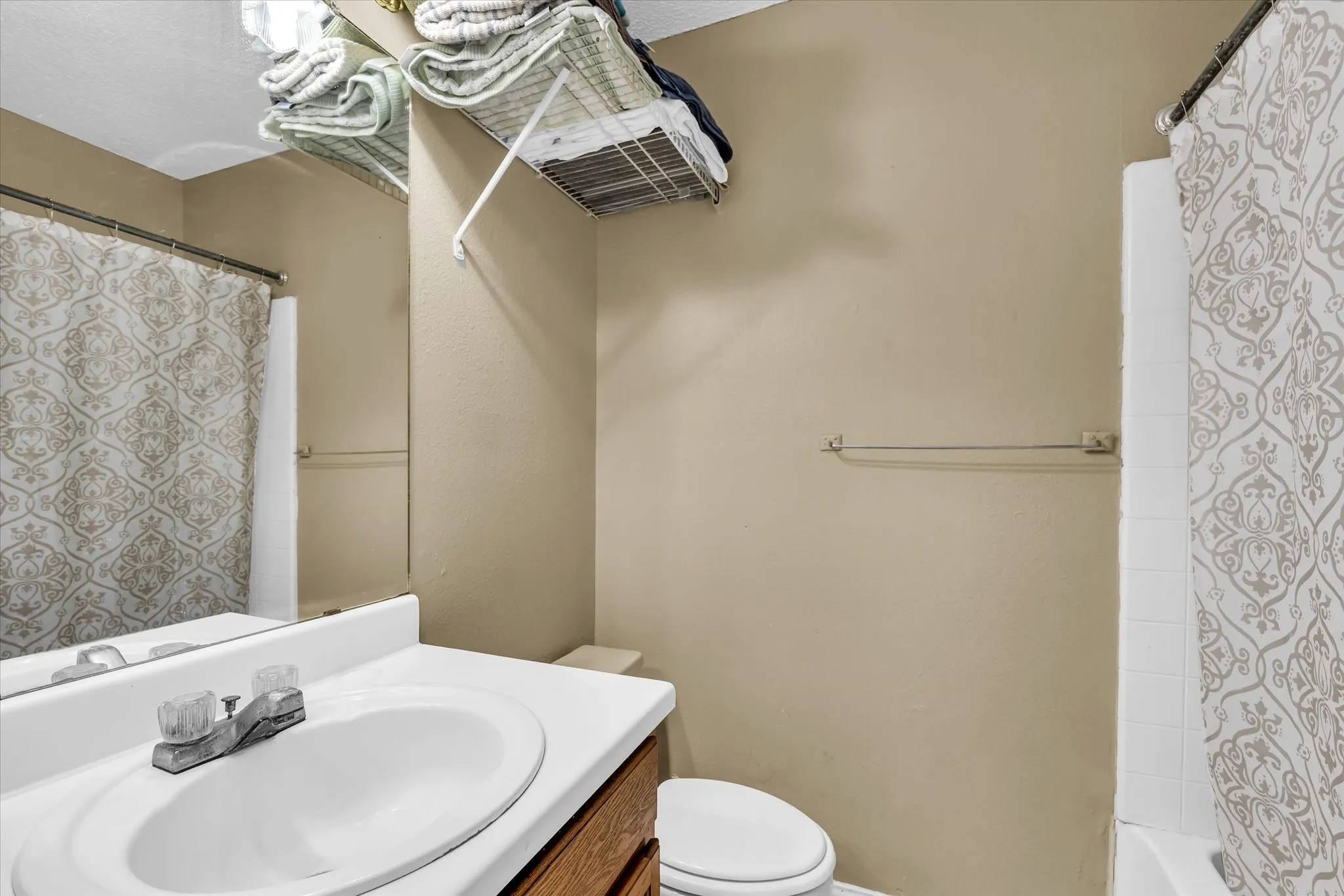 Bathroom featuring a white vanity with integrated sink, chrome faucet, wood-finish cabinetry, and a full-width mirror