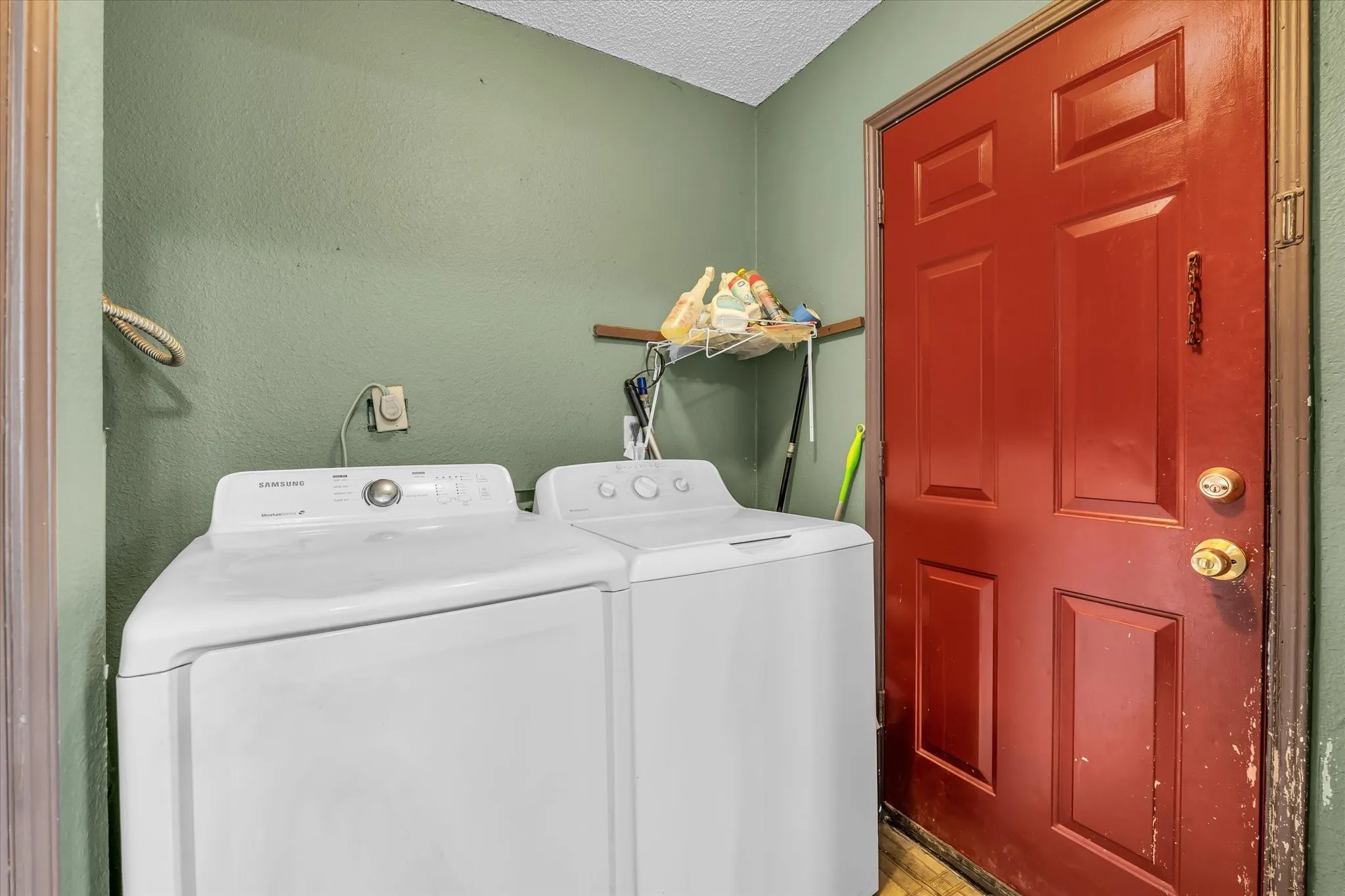 Utility area featuring a red paneled door, green painted walls, and textured ceiling