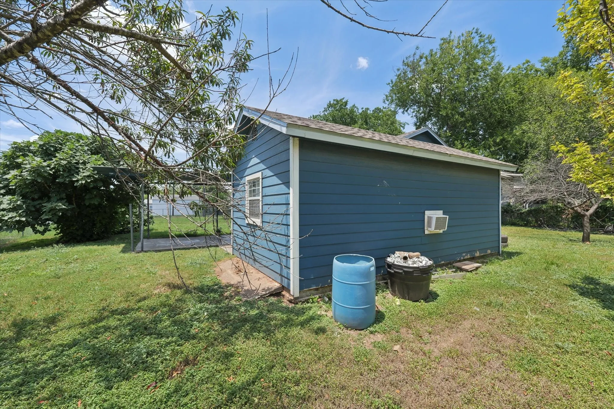 Detached structure featuring blue siding, white trim, a shingled roof, a single window, and a wall-mounted air conditioning unit