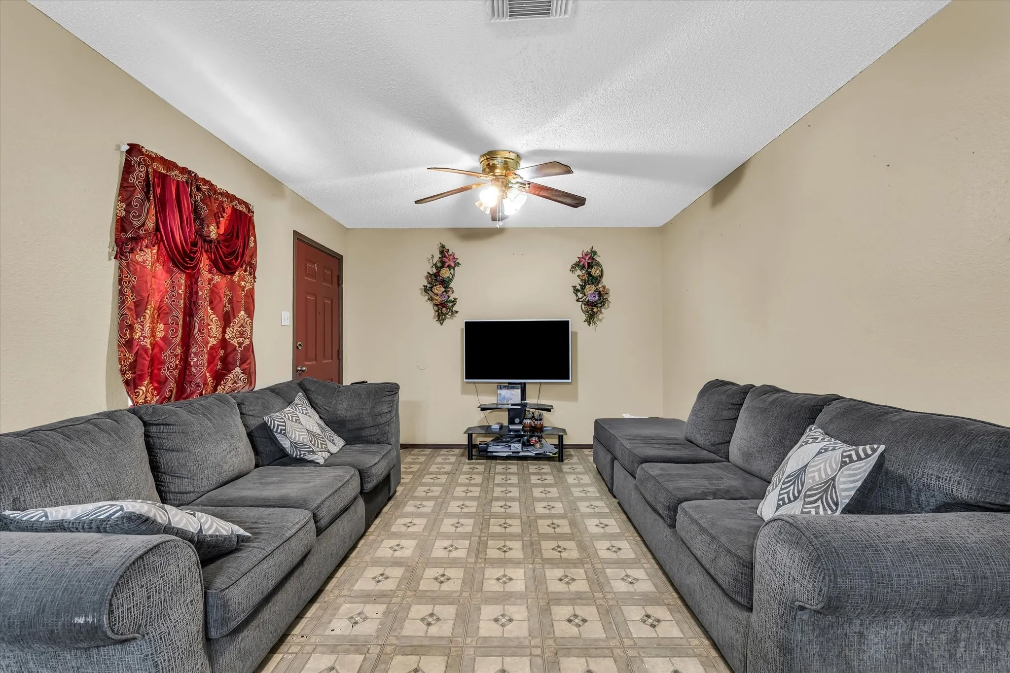 Living space featuring patterned tile flooring, light neutral wall tones, and a ceiling fan with integrated lighting