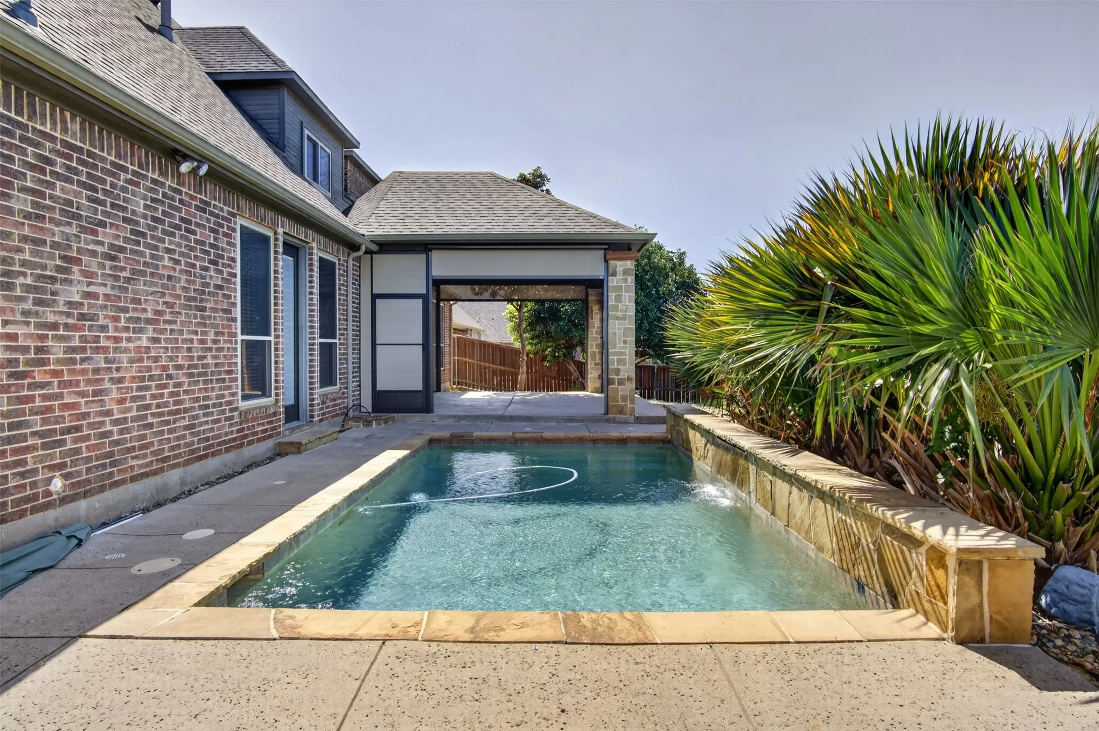 Resort-style saltwater pool with sun shelf and integrated spa jets, surrounded by stamped concrete decking