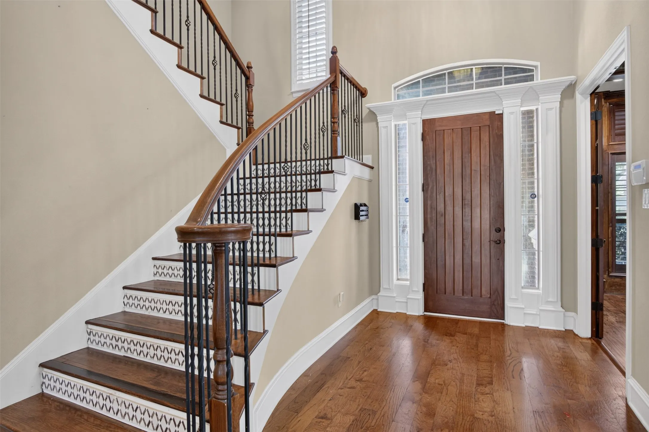 Hardwood flooring, custom wood entry door with transom window and sidelights, white paneled millwork, curved staircase with wood treads and wrought iron balusters