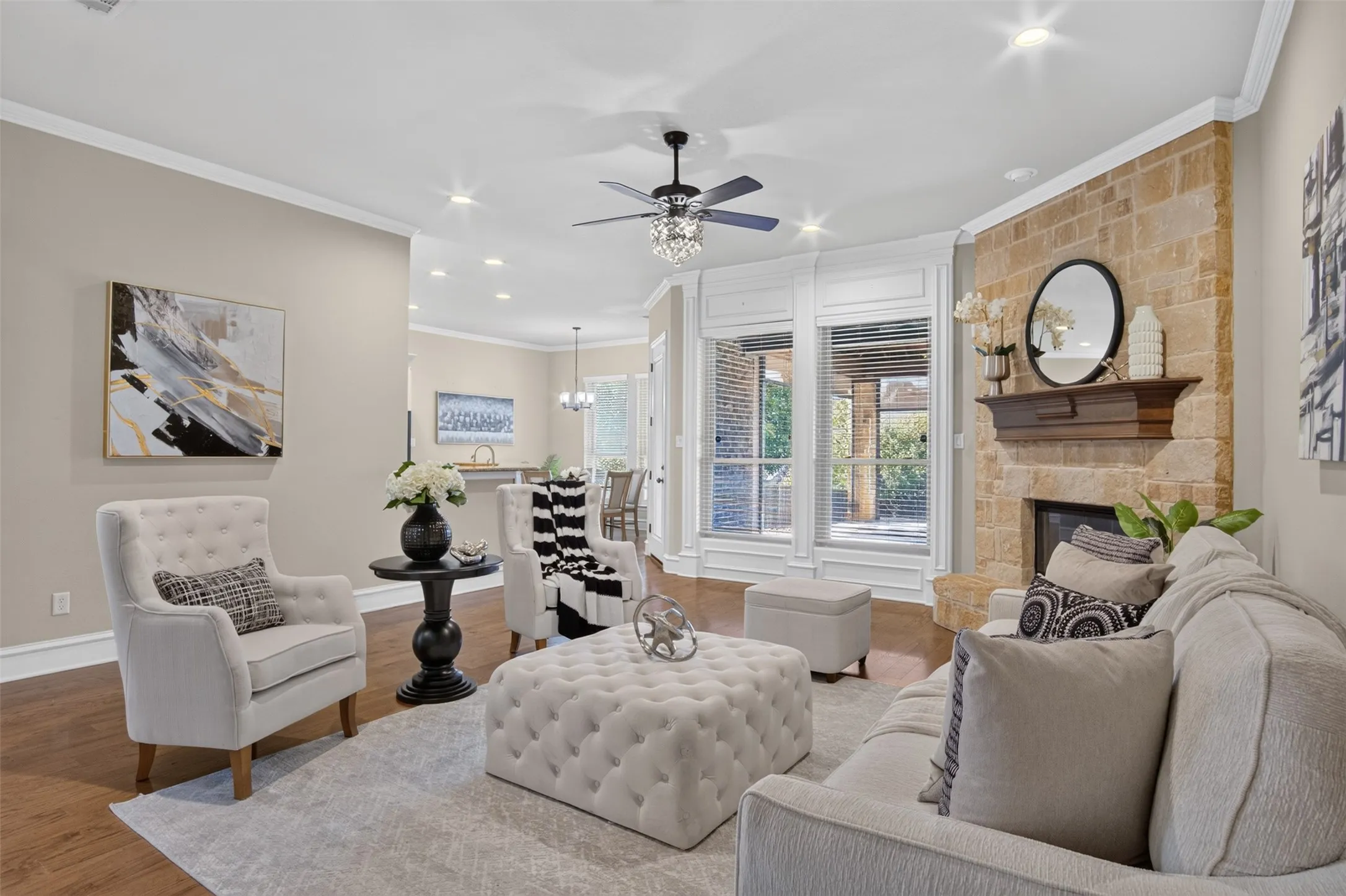 Recessed lighting, crown molding, wood-finish flooring, stone fireplace, and a ceiling fan with integrated lighting
