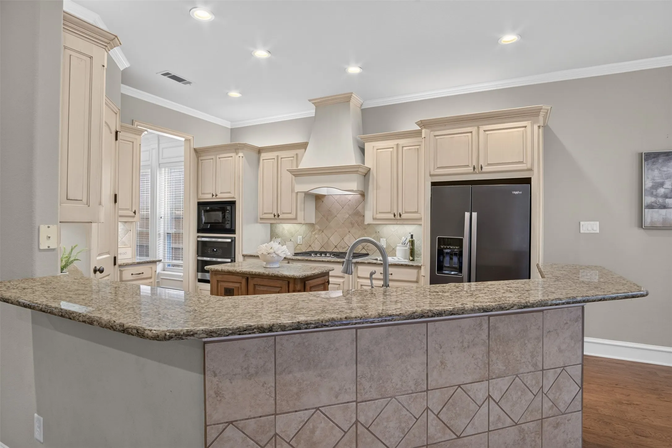 Kitchen featuring light-toned cabinetry, granite countertops, tile backsplash, built-in double ovens, and a center island with a wood-finish base
