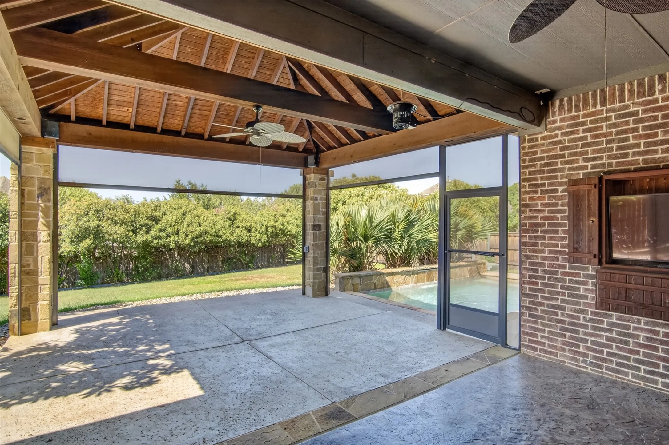 Covered patio featuring a wood-beam ceiling, stone columns, concrete flooring, and a brick exterior wall