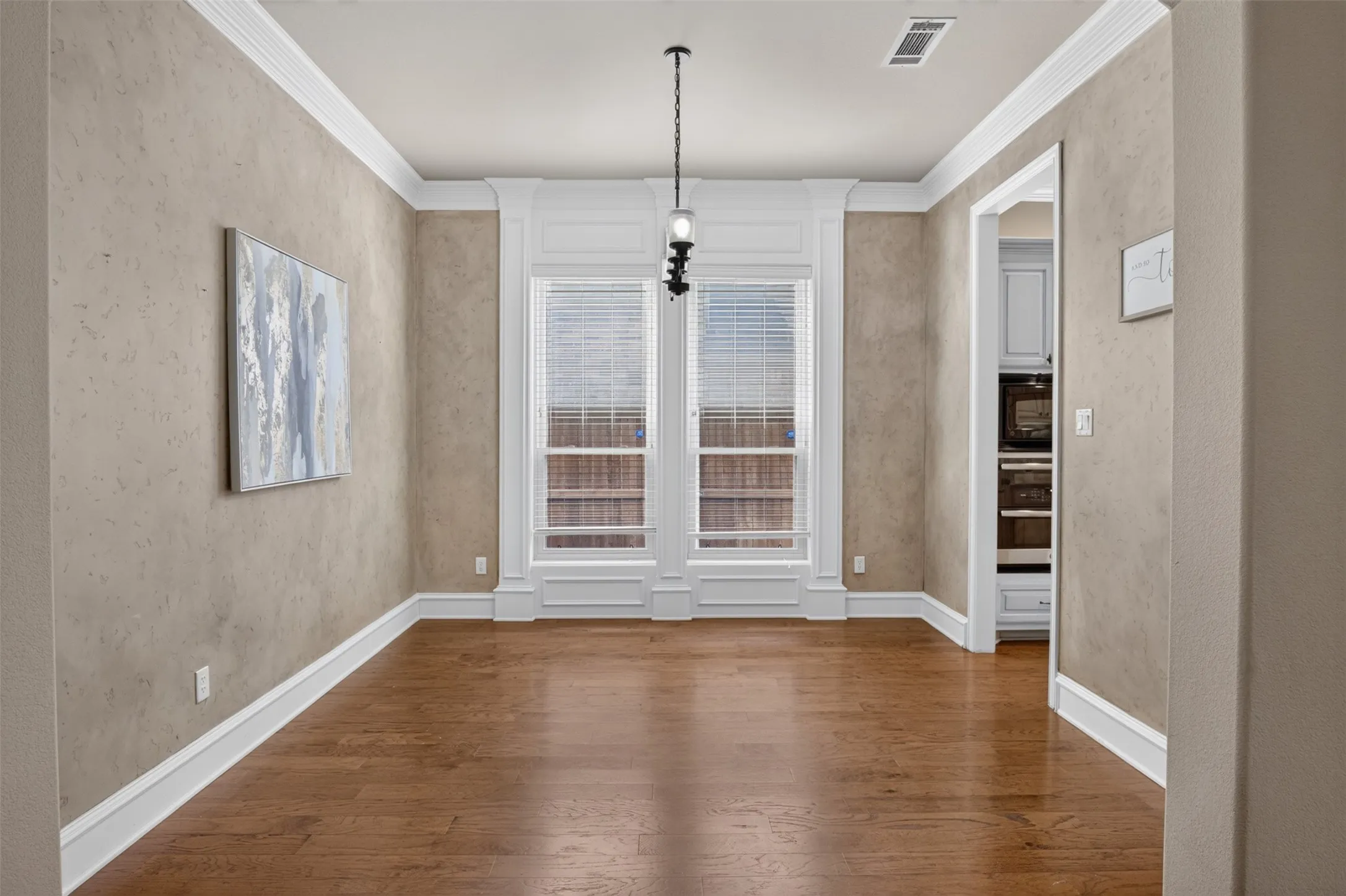 Hardwood flooring, textured wall finish, white crown molding, white window trim, and a built-in ceiling light fixture