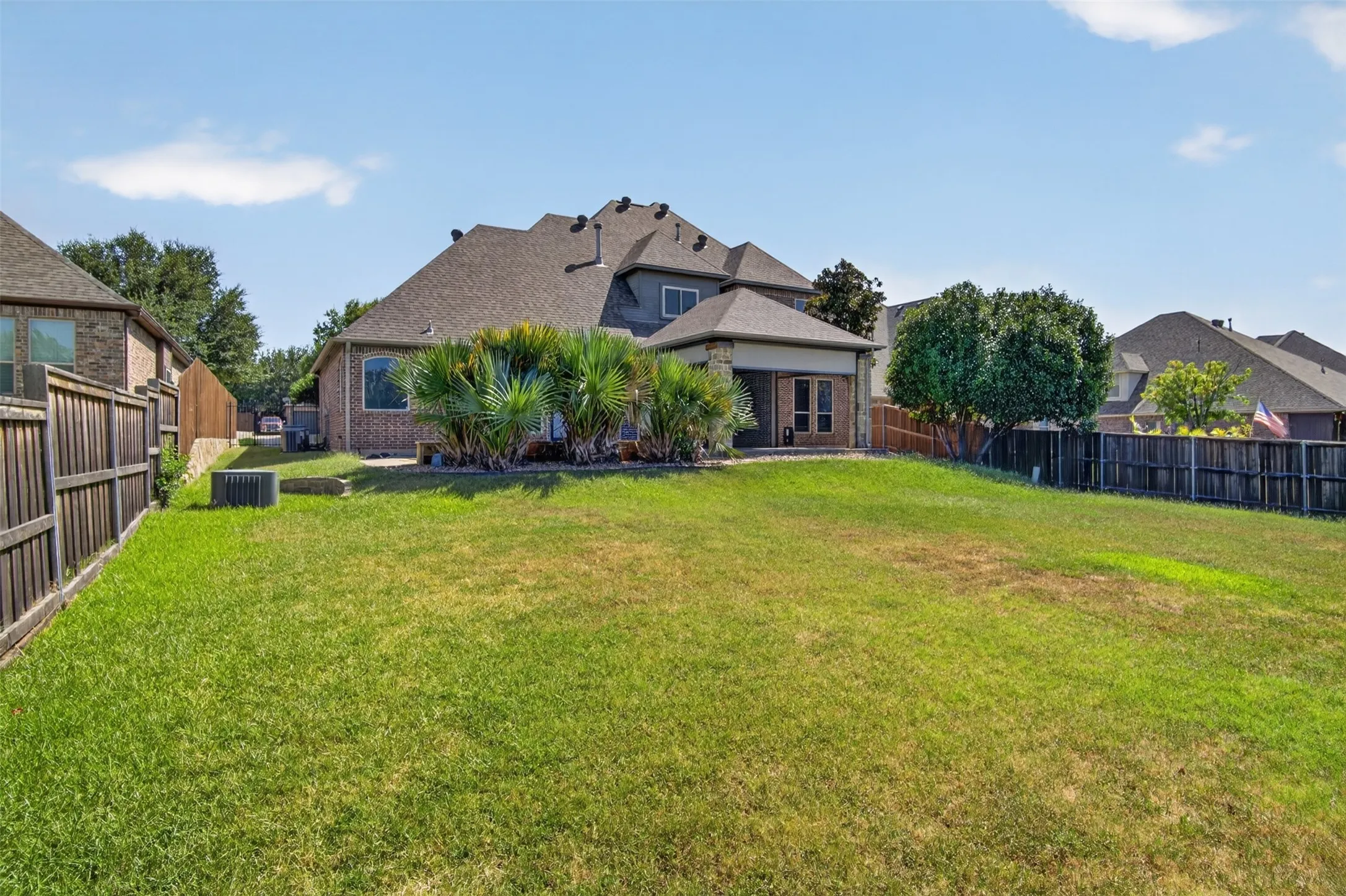 Expansive lawn with perimeter fencing, mature trees, and a covered patio