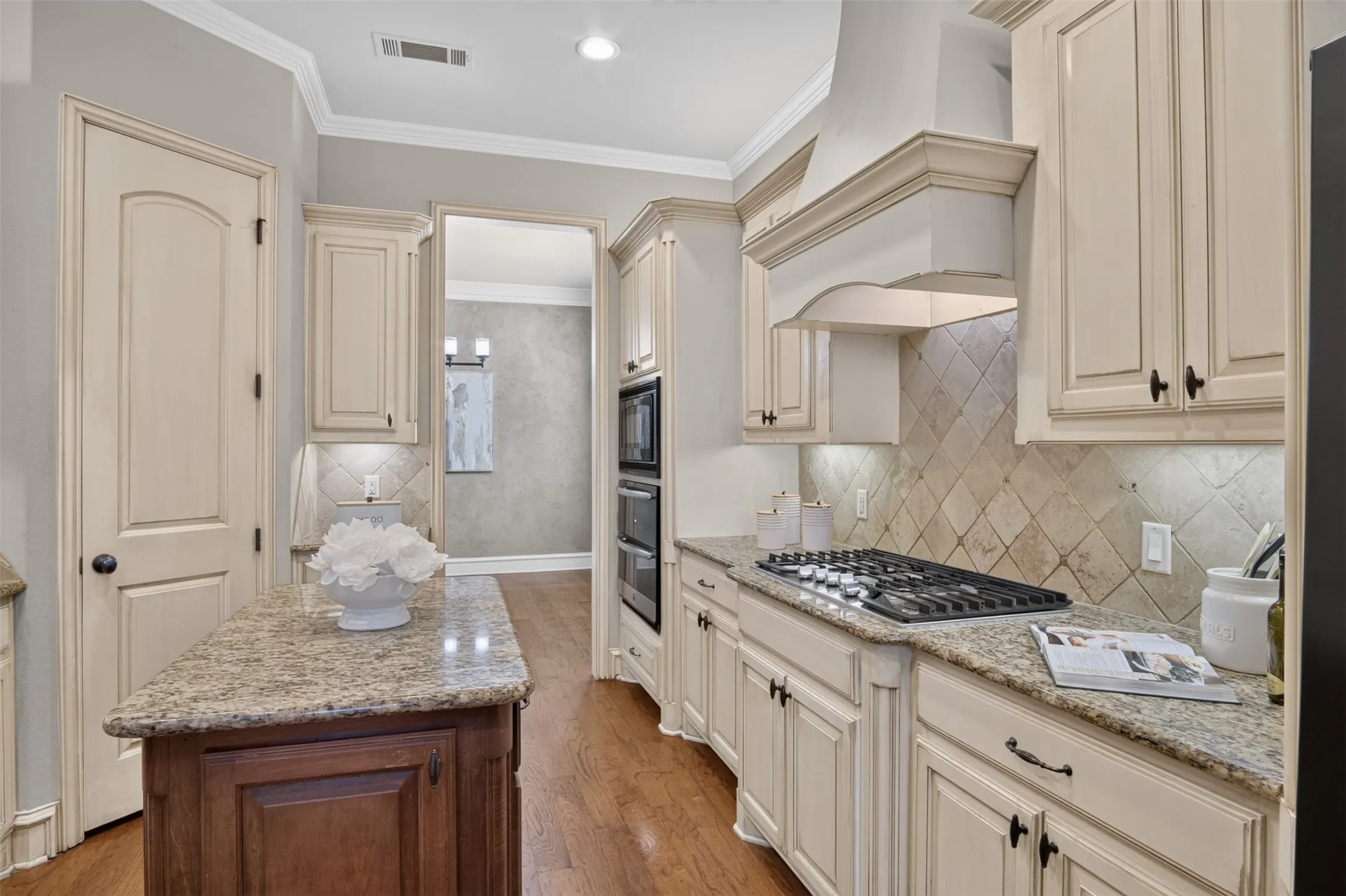 Elegant kitchen featuring cream-colored cabinetry with oil-rubbed bronze hardware, granite countertops, a six-burner gas cooktop, and a decorative tile backsplash