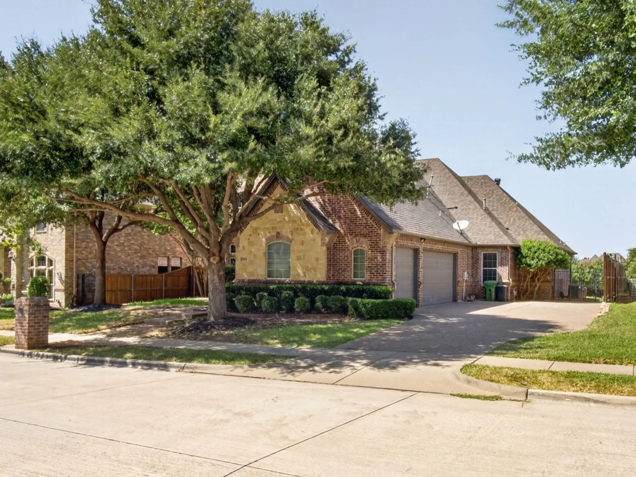 Brick and stone exterior featuring an attached garage, paved driveway, and mature landscaping