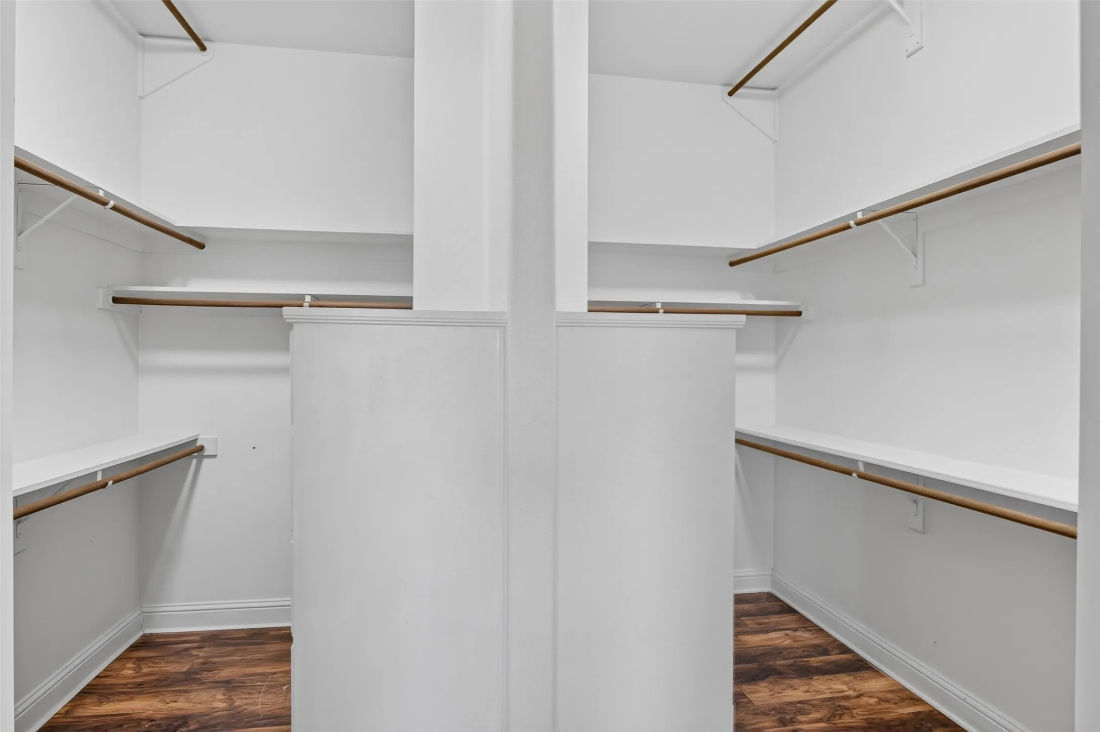 Walk-in closet featuring multiple shelving units, hanging rods, white walls, and wood-finish flooring