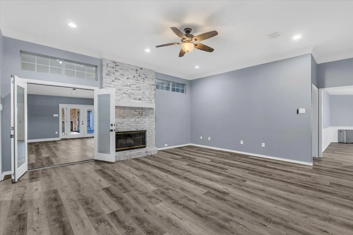 This expansive main living area is a true entertainer’s highlight, featuring sophisticated luxury vinyl plank flooring, a striking whitewashed brick fireplace, and elegant French doors that allow for a seamless flow into the adjoining room.