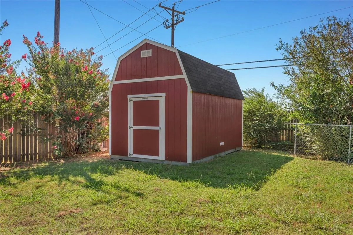The backyard features a spacious 10 x 20 red barn-style storage shed with crisp white trim and a built-in workbench, providing substantial additional space for lawn equipment, tools, or seasonal storage.