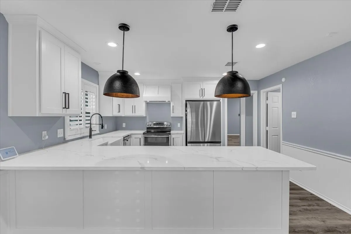 A clean, modern kitchen featuring crisp white cabinetry, premium quartz countertops, and dramatic oversized pendant lighting, creating a perfect space for both cooking and casual dining.