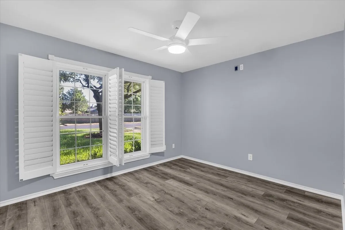 This is the first of five spacious bedrooms, offering a bright and versatile layout perfect for use as a guest suite or home office, featuring crisp paint, continuous luxury vinyl flooring, a modern lighted ceiling fan, and premium custom plantation shutters.