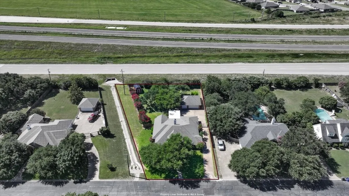This compelling aerial perspective highlights the property's expansive .57-acre lot, showcasing the generous outdoor space and deep setback from the street. The estimated boundary lines reveal the full scale of the grounds, easily accommodating the main residence, the long private driveway, the detached three-car garage, and beautiful mature shade trees, all backing up to a major roadway for ultimate commuting convenience.