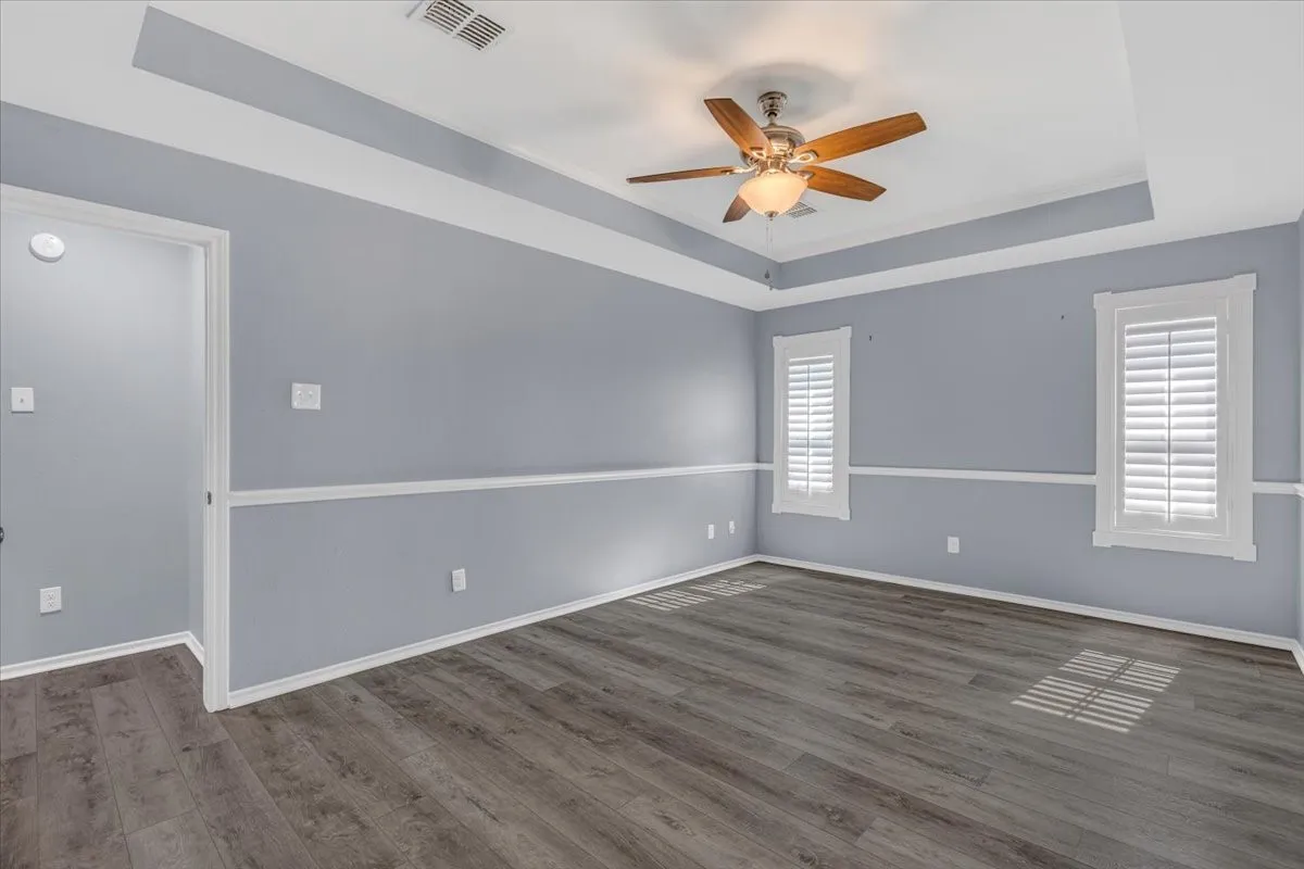 This expansive second primary suite provides a serene and versatile living space, enhanced by an elegant tray ceiling, classic chair rail molding, and high-quality luxury vinyl plank flooring. The room is perfectly complemented by custom plantation shutters, offering both sophisticated style and refined control over natural lighting.