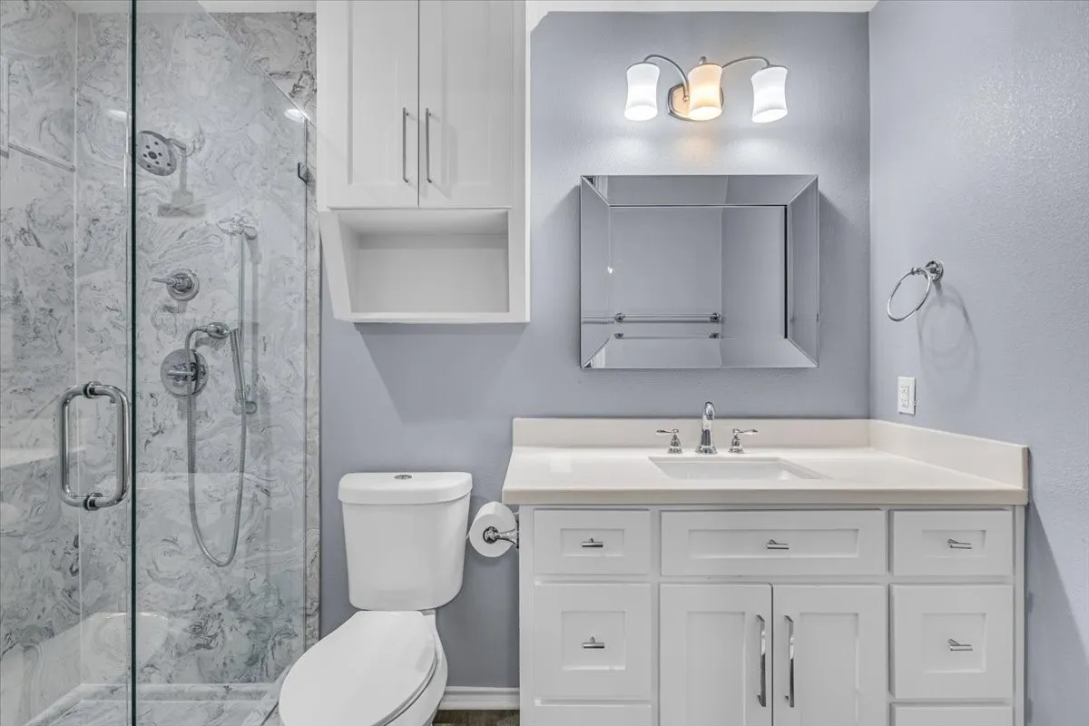 This beautifully updated guest bathroom features a clean white vanity, a modern mirror with stylish lighting, and an impressive walk-in shower finished with premium, high-contrast marble-style tile.