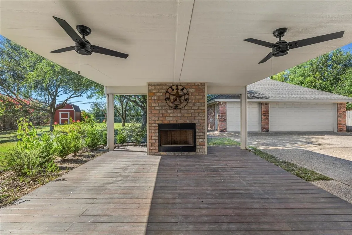 Step outside to an incredible covered outdoor living area, perfect for year-round entertaining. This space features a spacious wood deck, dual modern ceiling fans, and a striking central brick fireplace. The patio offers a relaxing vantage point overlooking the lush backyard, the charming red storage shed, and the expansive driveway leading to the detached three-car brick garage.
