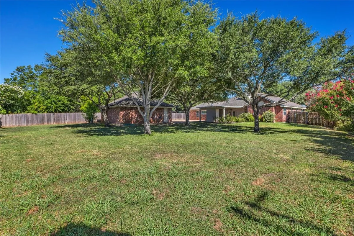 This spacious, park-like backyard offers a sprawling lawn beautifully shaded by magnificent mature trees. The generous lot provides endless possibilities for outdoor living and entertainment, complete with vibrant blooming crepe myrtles, privacy fencing, and clear views of the home's covered patio and detached brick garage.