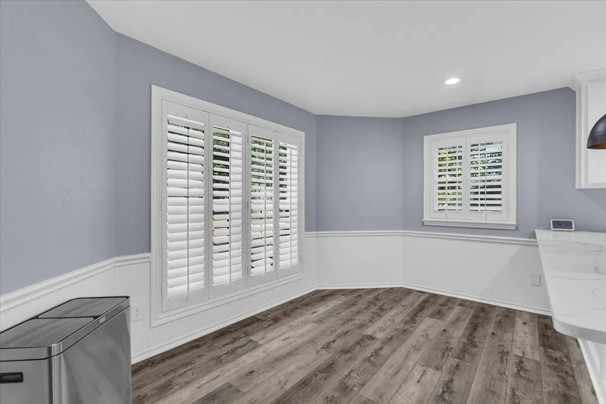 Inviting breakfast nook featuring elegant wainscoting, continuous luxury vinyl plank flooring, and custom plantation shutters that provide a sophisticated touch and excellent natural light control.