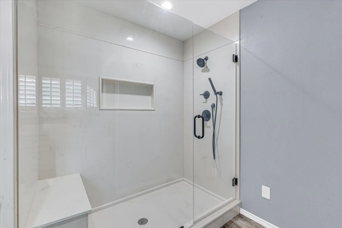 This beautifully updated primary walk-in shower features premium large-format tile, a convenient built-in bench, a custom recessed niche for storage, and a sleek modern shower system with matte black hardware.