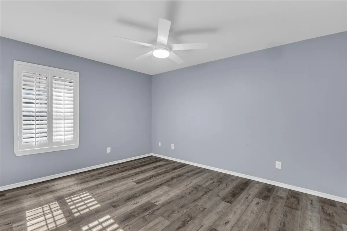This is the second of five spacious bedrooms, offering a bright and comfortable space featuring crisp paint, continuous luxury vinyl flooring, a modern lighted ceiling fan, and premium custom plantation shutters.